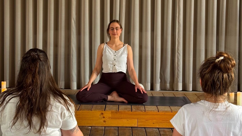 Lena Horenkamp meditiert im Schneidersitz auf der Bühne im flow, zwei Teilnehmerinnen sitzen ihr gegenüber